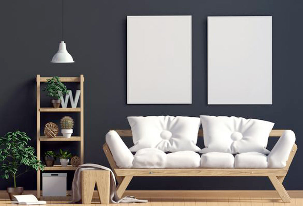 A wooden couch with white cushions in front of a dark grey painted wall, with a wooden shelf beside with green plants.