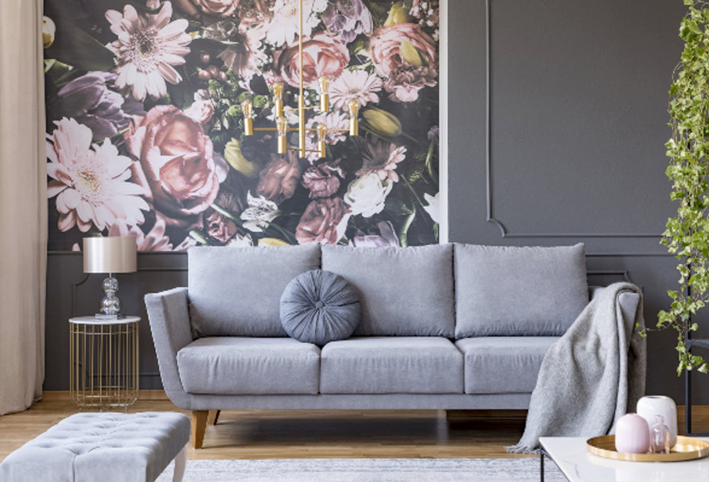 Grey couch in front of a dark black wall with floral wallpaper.