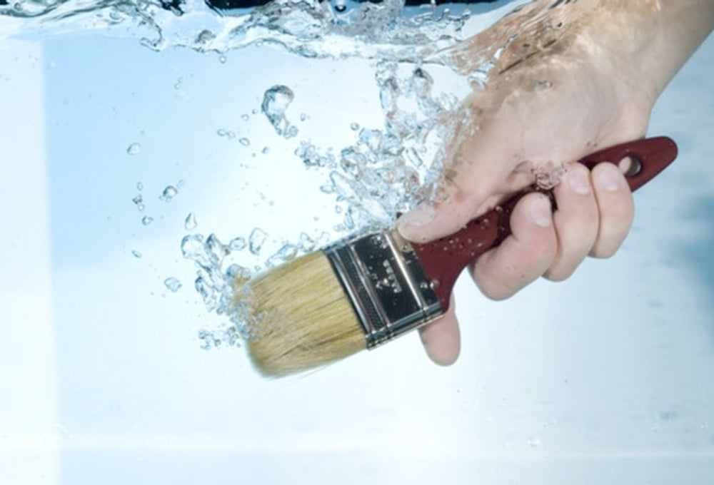 A person's hand holding a paint brush under water.