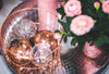 Gold and silver holiday ornaments in a gold basket, next to a pink holiday poinsetta.