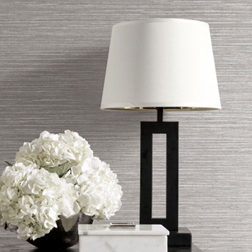 A white bouquet of flowers and a lamp with a white lamp shade, on a table in front of a wall with like grey textured wallquest wallpaper.
