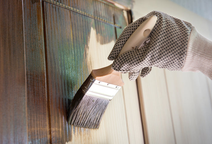 A person's hand wearing a glove and using a paint brush to stain wood.