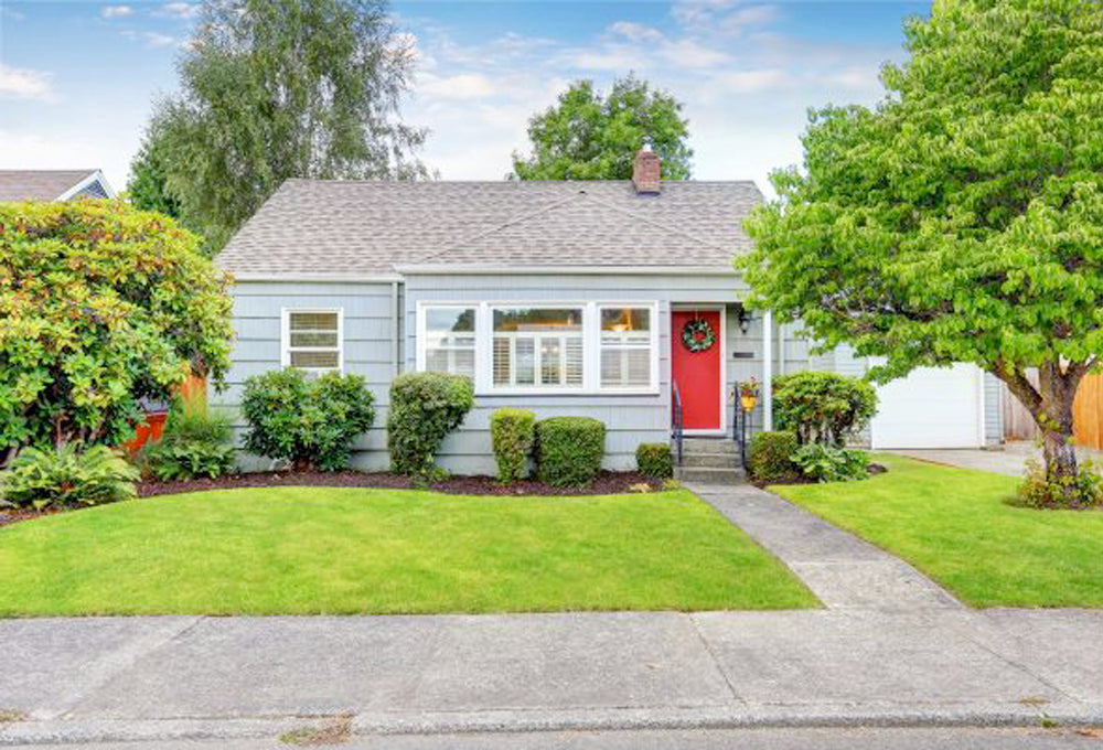 Light blue house with a bright red front door, with green bushes and trees in front.