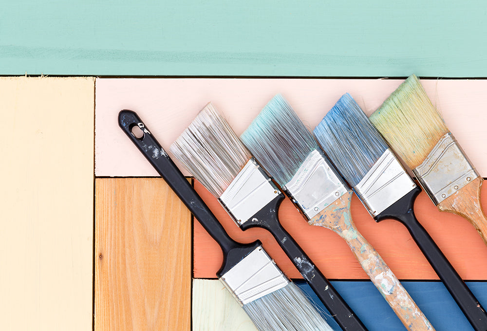 Five paint brushes side by side on top of colored wood pieces.