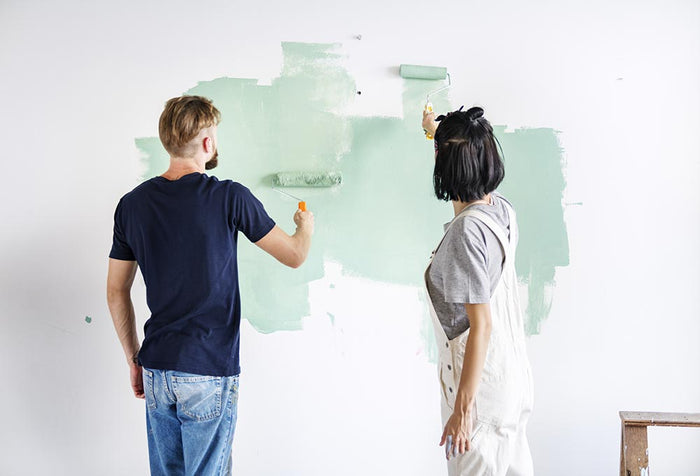 A man and woman painting a wall using mint green colored paint.