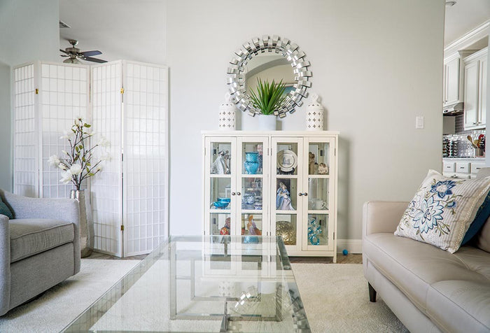 Living room with a taupe leather couch, beige carpet and glass-top coffee table, with a china cabinet. 