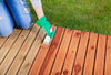 A person staining a deck, wearing green gloves.