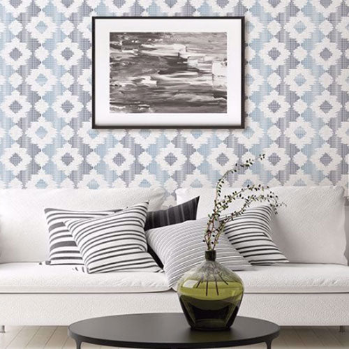 A white couch with black and white pillows in front of a wall with a blue and grey patterned wallpaper from Brewster.