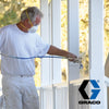 A man in a white t shirt and white pants wearing a respirator mask using a Graco airless paint sprayer on a white porch.