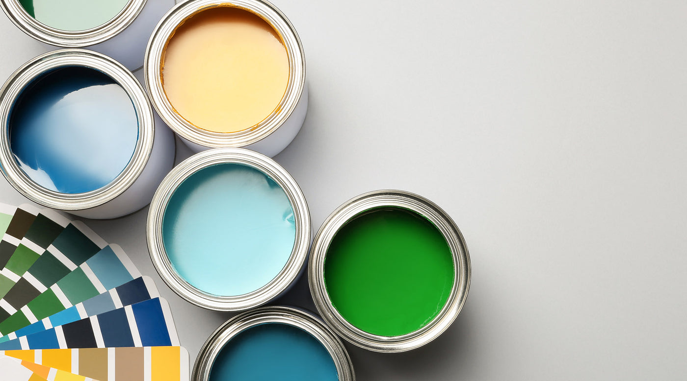 An aerial view of fanned out green, blue and yellow paint color chips, with open paint gallons showing blue, yellow and green paint inside of them.