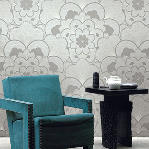 A teal suede chair and black side table, in front of a wall with wallquest wallpaper with a grey floral pattern called 