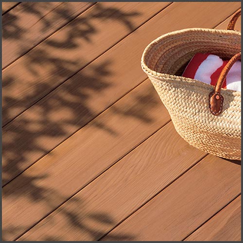 A wooden deck stained with Benjamin Moore's Arborcoat, with a straw beach bag sitting on the deck. 
